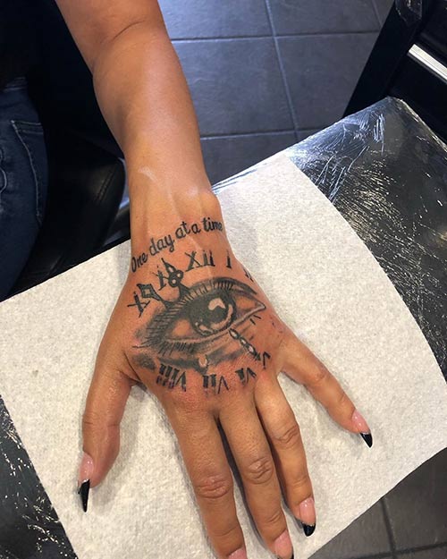 Artsy hand tattoo with eye roman numerals and script for hand tattoo design